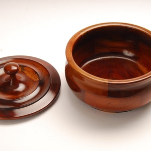 May include: A wooden bowl with a lid. The bowl is made of dark wood and has a smooth, polished finish. The lid has a knob on top.