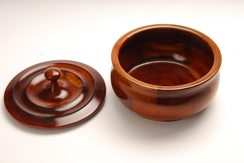 May include: A wooden bowl with a lid. The bowl is made of dark wood and has a smooth, polished finish. The lid has a knob on top.