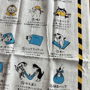 Può includere: Un asciugamano rettangolare bianco con un bordo a strisce di pericolo nere e gialle. Il tessuto mostra diciassette illustrazioni numerate di gatti che dimostrano vari usi dell'asciugamano, accompagnate da istruzioni in testo giapponese per ciascuna.