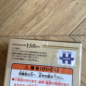 May include: A mini puzzle box with the text "mini puzzle 150 pcs." is displayed. The box has Japanese text and a sample puzzle piece sticker. The box is tan and white.