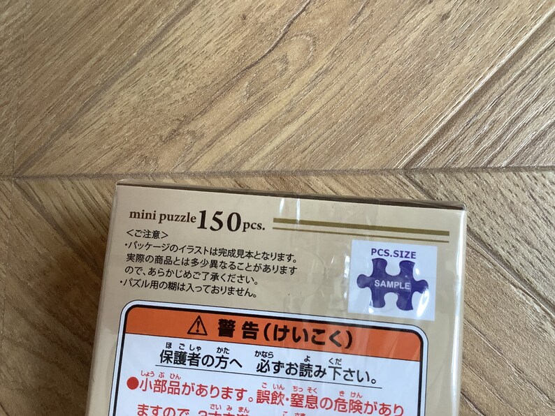 May include: A mini puzzle box with the text "mini puzzle 150 pcs." is displayed. The box has Japanese text and a sample puzzle piece sticker. The box is tan and white.