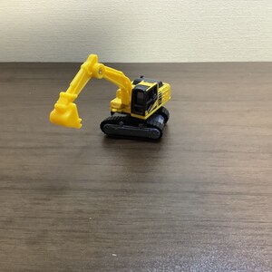 May include: A yellow and black toy excavator with a movable arm and bucket. The toy is on a wooden surface. The excavator has black tracks and a detailed cabin. A fun toy for kids.