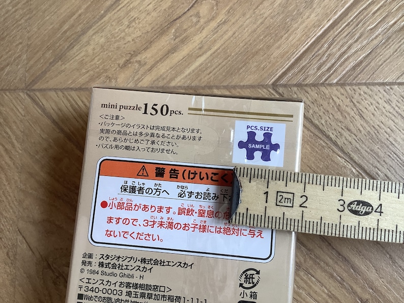 May include: A mini puzzle box with the text "mini puzzle 150 pcs." and Japanese text. A ruler is placed next to the box. The box has a sticker that says "PCS.SIZE SAMPLE".