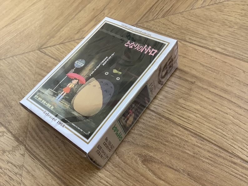 May include: A boxed Studio Ghibli poster collection featuring the animated film "My Neighbor Totoro." The box art depicts a scene with Totoro, a girl with an umbrella, and a bus stop. Released in 1988. The box size is 10 x 14.2 cm.
