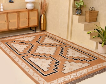 May include: A rectangular area rug featuring a tan base with a repeating geometric pattern in cream and black, finished with a fringed edge. The rug displays the text RUGSEXPORTS in the bottom right corner, set against a neutral interior.