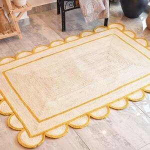 May include: A white and yellow jute rug with a scalloped edge. The rug has a double yellow border.