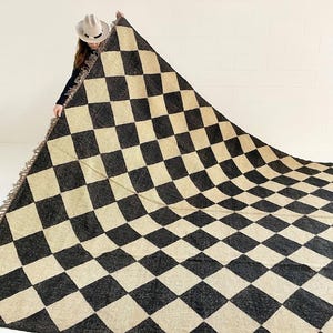 Può includere: Un tappeto a scacchi bianco e nero con un bordo a frangia. Il tappeto è realizzato in materiale tessuto e presenta un motivo geometrico.