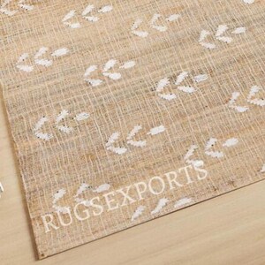 May include: A beige and white area rug with a woven texture and a white arrow pattern. The rug has the text "RUGSEXPORTS" printed on it.