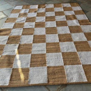 May include: A woven rug with a checkered pattern in brown and white. The rug is made of natural fibres and has a rustic look.
