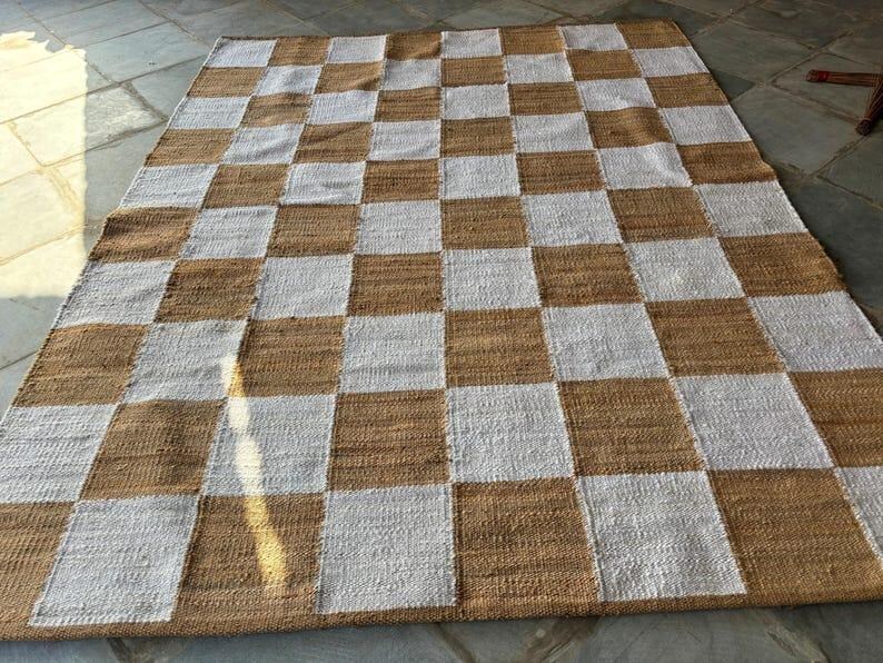 May include: A woven rug with a checkered pattern in brown and white. The rug is made of natural fibres and has a rustic look.