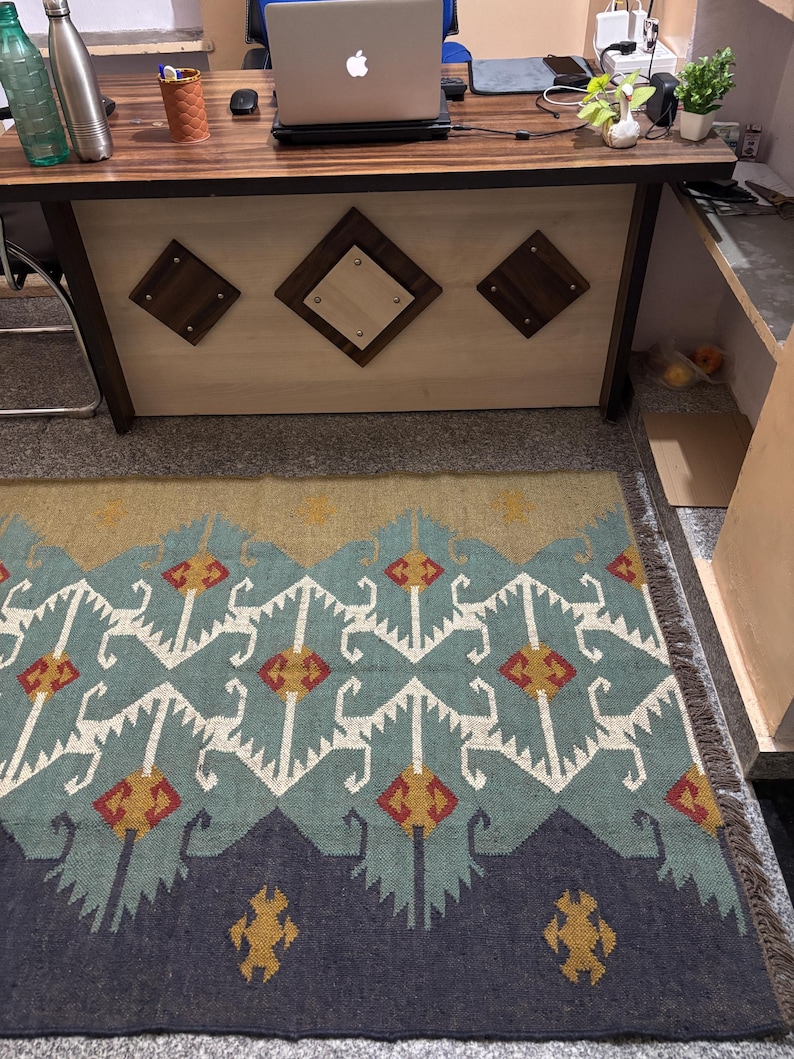May include: A blue, white, red, and yellow patterned rug with fringe. The rug has a geometric design and is laid out on a tiled floor.
