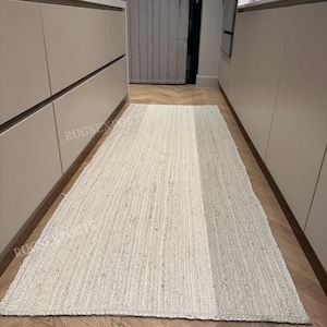 Può includere: Un tappeto da corridoio in juta bianca con una texture sottile. Il tappeto è steso su un pavimento in legno in un corridoio tra due set di armadi.