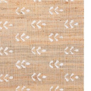 May include: A close-up of a natural fiber rug with a white arrow pattern. The rug has a light brown color and a woven texture.