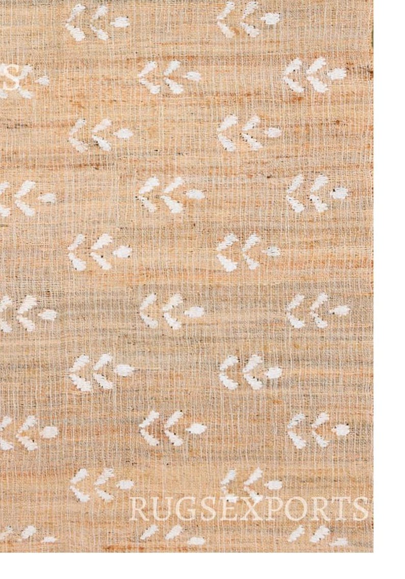 May include: A close-up of a natural fiber rug with a white arrow pattern. The rug has a light brown color and a woven texture.