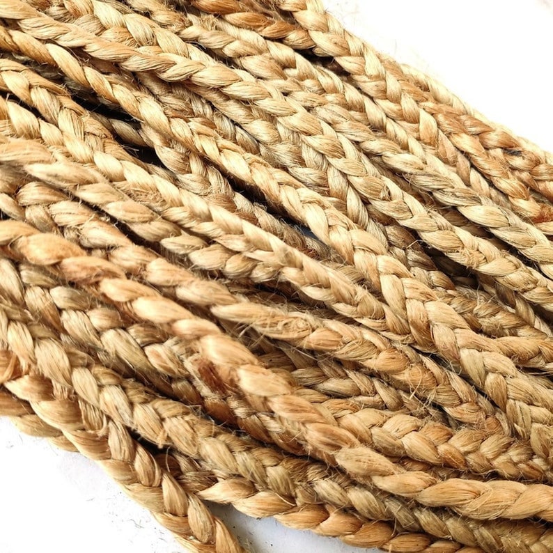 May include: Close-up of several strands of braided jute rope. The rope is a natural tan color, with visible texture and variations in tone. The braids are tightly woven, creating a sturdy and durable appearance. The rope is likely used for crafting or decorative purposes.
