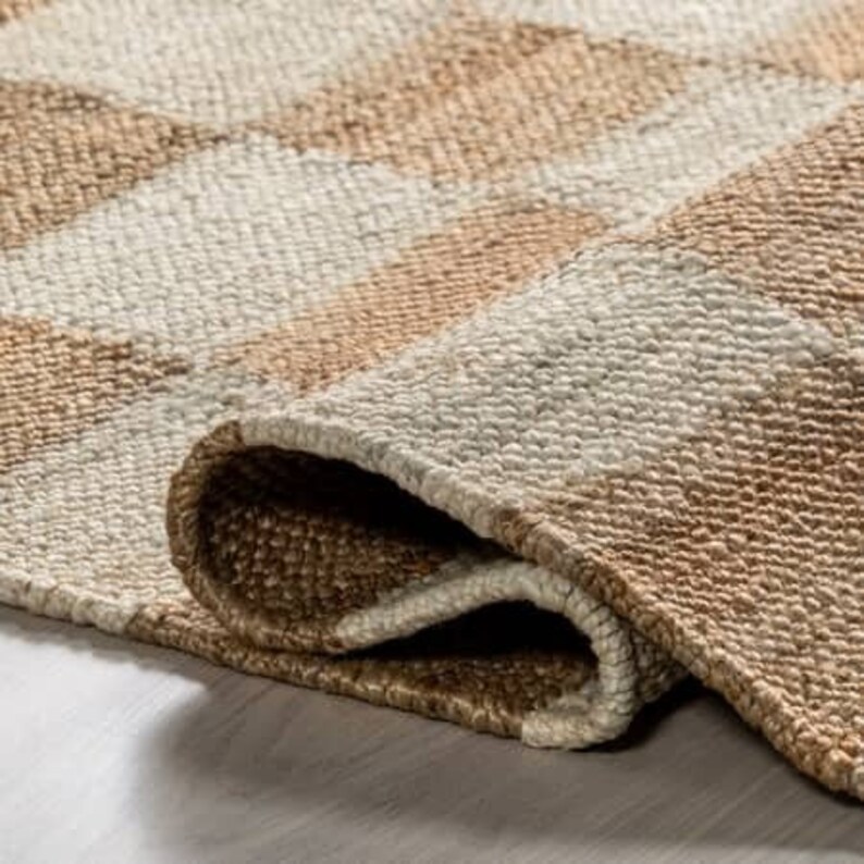 May include: Close-up of a woven rug with a striped pattern in beige and white. The rug is folded over, showing the texture of the weave.