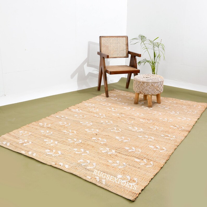 May include: A natural fiber rug with a white floral pattern on a beige background. The rug is displayed with a wooden chair and a white stool.