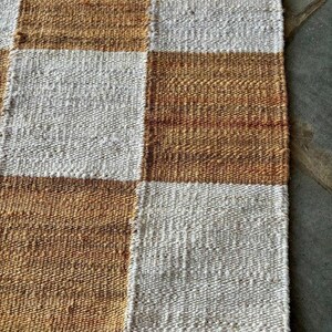 May include: A woven rug with a checkered pattern in brown and white. The rug is made of natural fibres and has a rustic look.