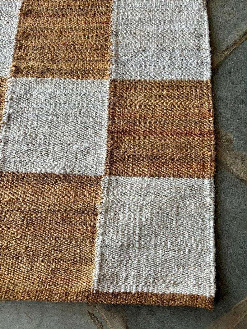 May include: A woven rug with a checkered pattern in brown and white. The rug is made of natural fibres and has a rustic look.