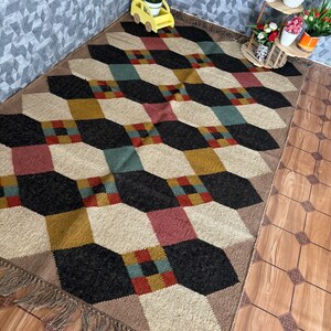 Pu&ograve; includere: Tappeto a motivi geometrici con un motivo a cubo ripetuto in nero, beige, rosso, verde acqua e oro. Il tappeto ha un bordo con frange ed &egrave; posizionato su un pavimento in legno. Un elemento decorativo per la casa.