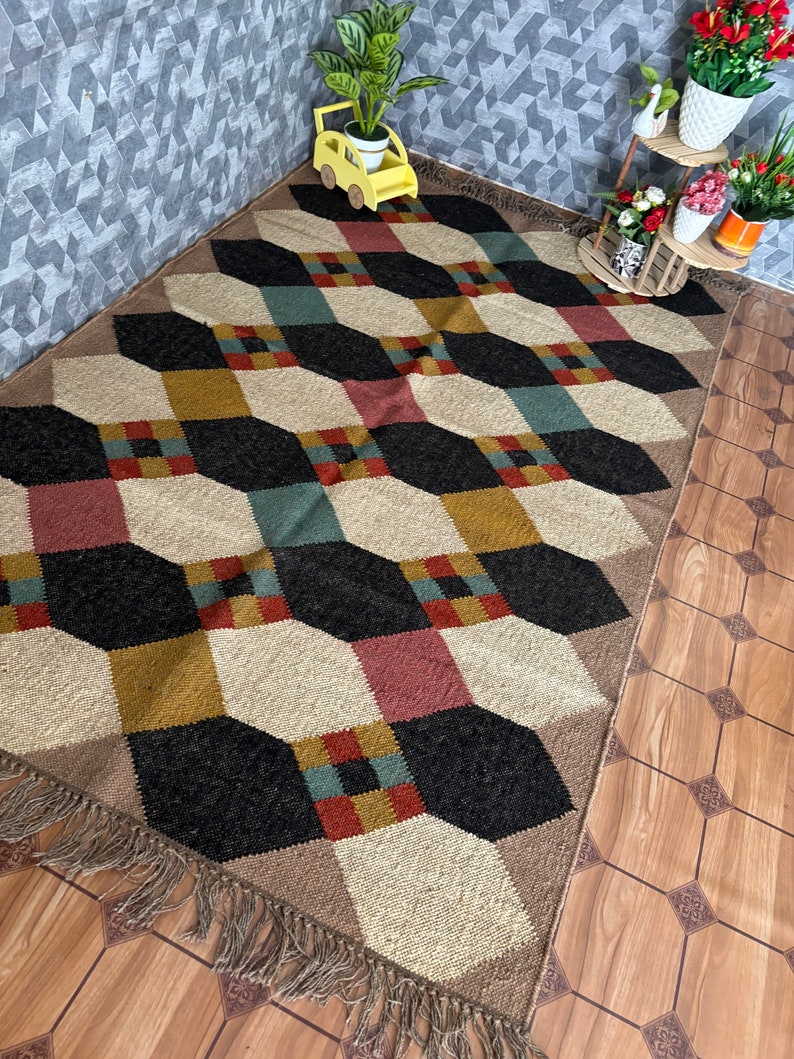 Pu&ograve; includere: Tappeto a motivi geometrici con un motivo a cubo ripetuto in nero, beige, rosso, verde acqua e oro. Il tappeto ha un bordo con frange ed &egrave; posizionato su un pavimento in legno. Un elemento decorativo per la casa.