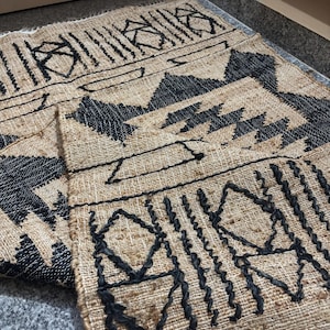 May include: A black and brown woven rug with a geometric pattern. The rug has a fringe border and the text "RUGSEXPORTS" is visible in the bottom right corner.