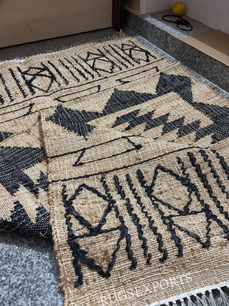 May include: A black and brown woven rug with a geometric pattern. The rug has a fringe border and the text "RUGSEXPORTS" is visible in the bottom right corner.
