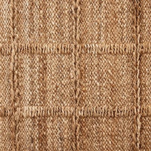 May include: Close-up of a woven jute rug with a natural brown color and a textured, slightly rough surface. The rug has a grid pattern created by thicker woven lines.