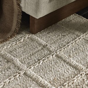 May include: A light gray woven rug with a textured, braided design. The rug has a subtle pattern of horizontal stripes.