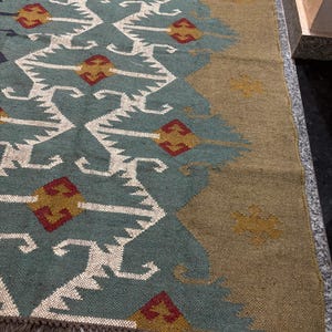 May include: A teal and brown patterned rug with a geometric design. The rug has a fringe border and is made of woven fibers.
