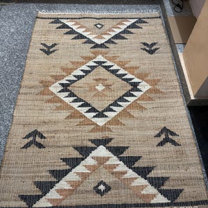 May include: A brown and black geometric patterned rug with a fringe border. The rug has a tribal design with black, white, and brown triangles and diamonds.