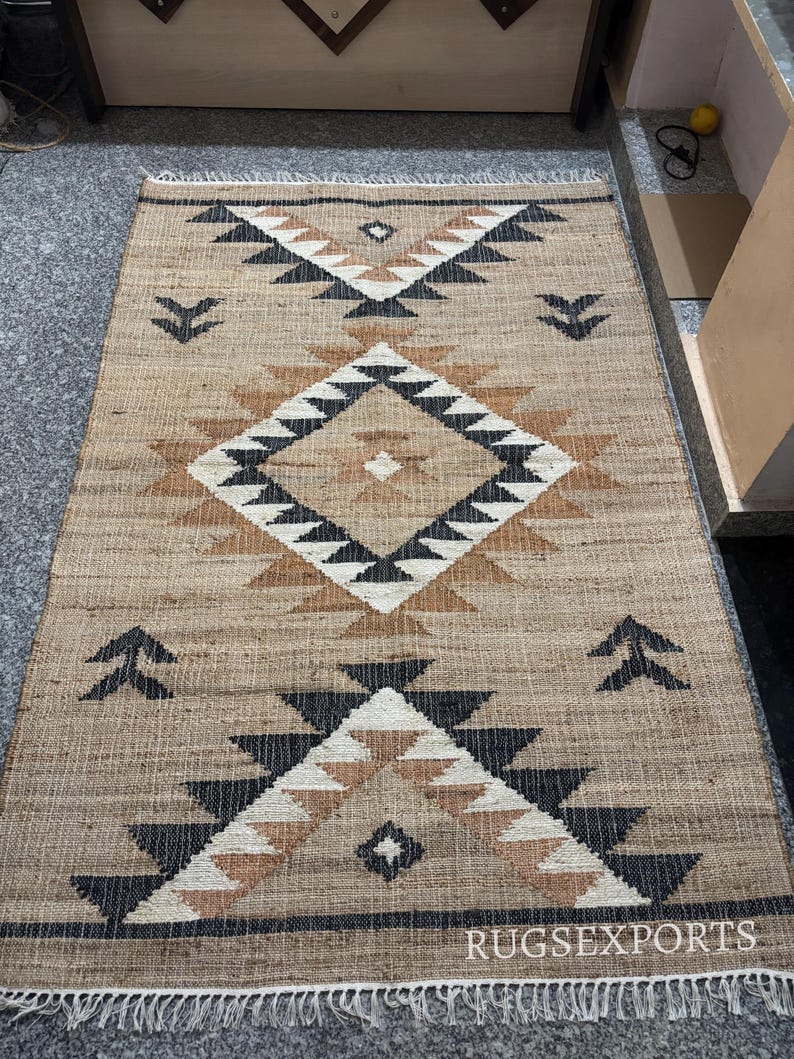 May include: A brown and black geometric patterned rug with a fringe border. The rug has a tribal design with black, white, and brown triangles and diamonds.