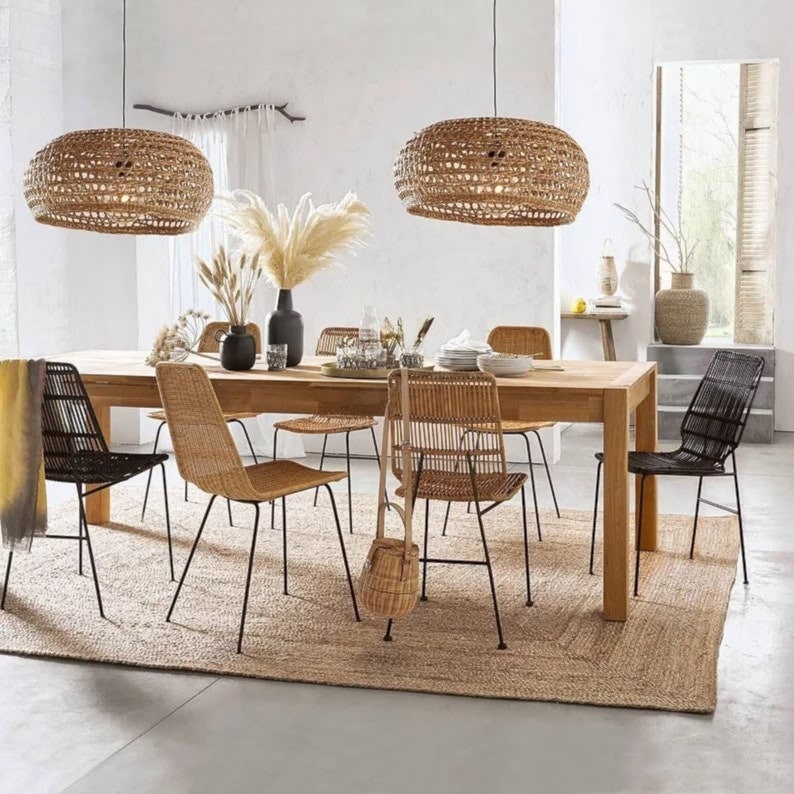 K&ouml;nnte beinhalten: Ein Esstisch mit sechs St&uuml;hlen, einem gewebten Teppich und zwei gewebten Pendelleuchten. Der Tisch ist aus Holz und die St&uuml;hle sind aus schwarzem Metall mit gewebten Sitzen. Der Teppich ist aus Naturfasern und die Leuchten sind aus gewebtem Rattan.