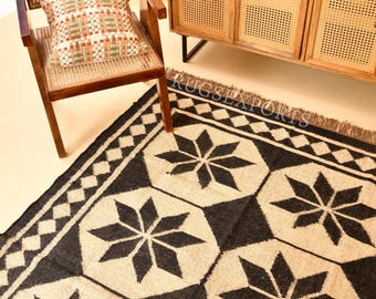 May include: A rectangular area rug featuring a repeating pattern of black eight-pointed stars on a natural beige background, bordered by a black and beige diamond chain design. The rug has a textured weave and includes a fringe along the edge.