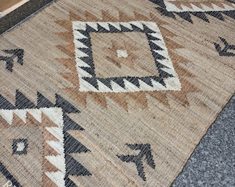 May include: A rectangular woven rug featuring a natural tan base with a geometric pattern in black, white, and brown. The design includes large diamonds and small arrow-like motifs. The text RUGSEXPORTS is visible in the bottom corner.