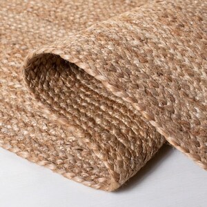 K&ouml;nnte beinhalten: Nahaufnahme eines Naturfaser-Teppichs aus gewebtem Jute. Der Teppich hat eine hellbraune Farbe und eine strukturierte Oberfl&auml;che.