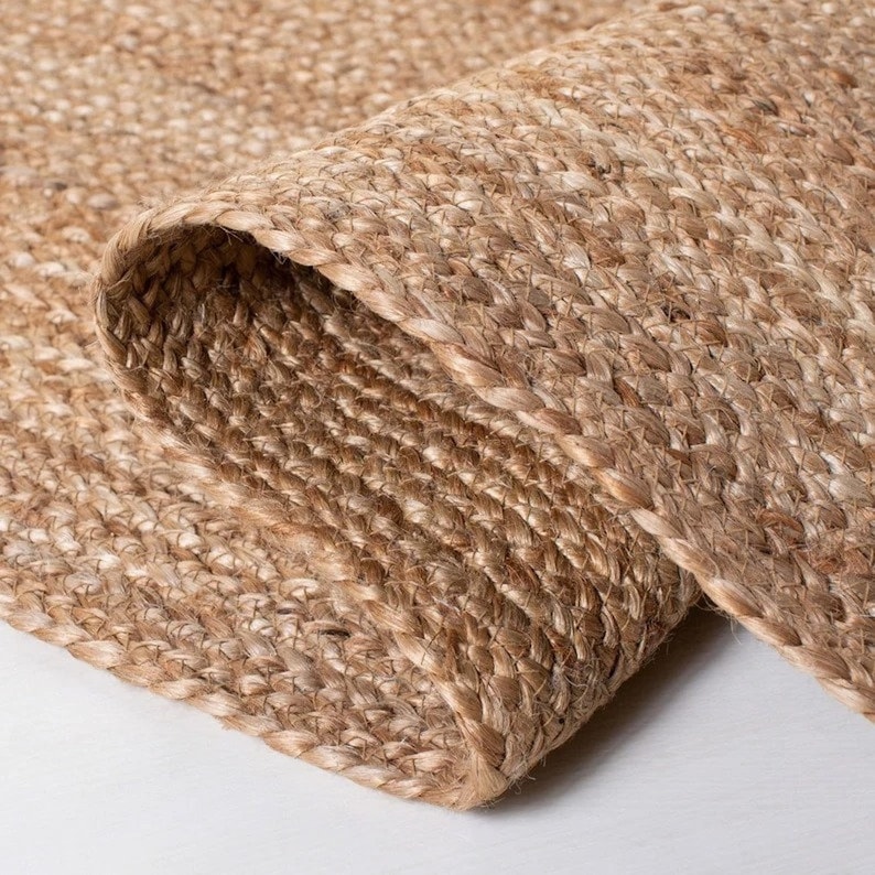 K&ouml;nnte beinhalten: Nahaufnahme eines Naturfaser-Teppichs aus gewebtem Jute. Der Teppich hat eine hellbraune Farbe und eine strukturierte Oberfl&auml;che.