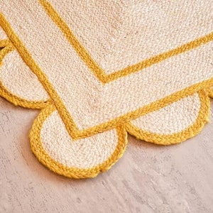 May include: A white and yellow jute rug with a scalloped edge. The rug has a double yellow border.