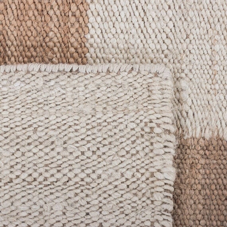 May include: Close-up of a woven rug with a beige and brown colour scheme. The rug has a textured, hand-woven look.