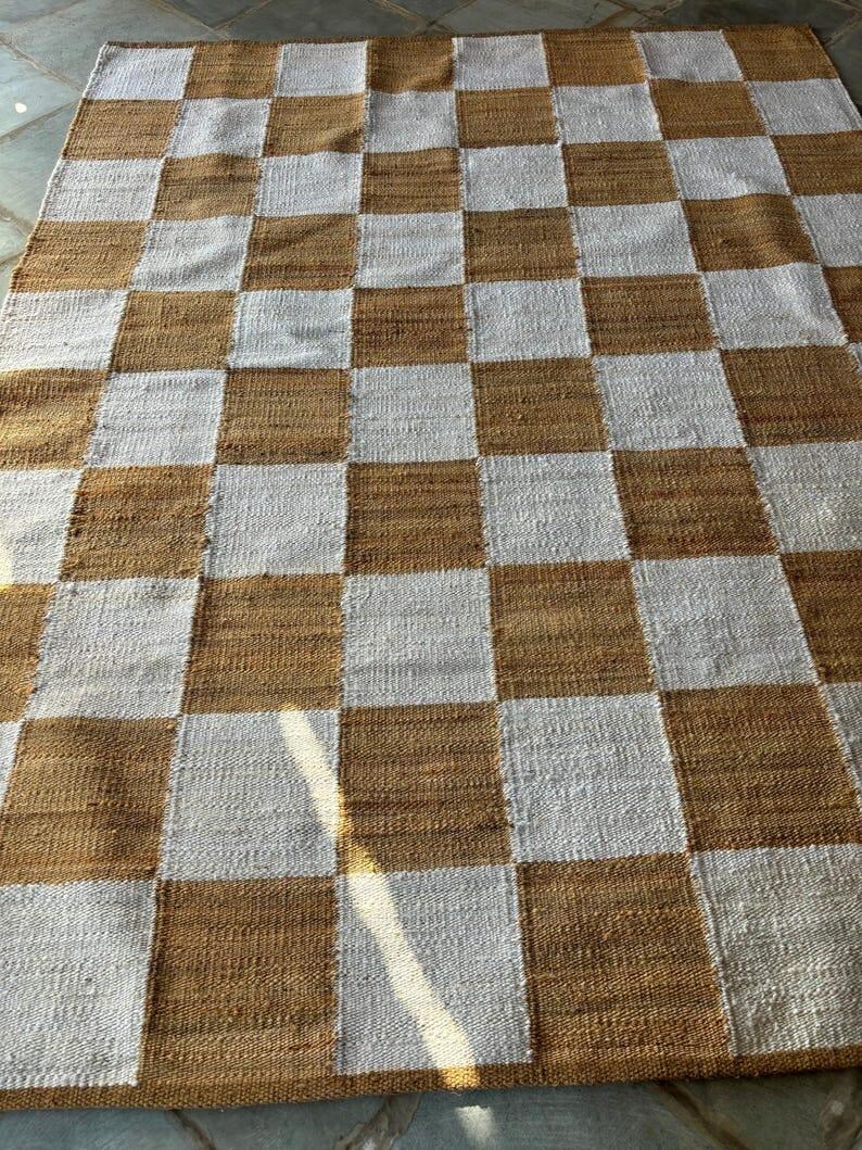 May include: A checkered rug with alternating squares of brown and white. The rug is made of a woven material and has a slightly textured surface.