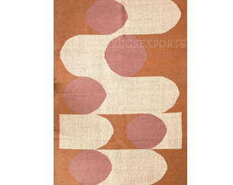 May include: A rectangular area rug featuring a burnt orange background with a repeating pattern of cream-colored elongated shapes and dusty rose circles. The rug has a woven texture and is finished with short, light-colored fringe on both ends.