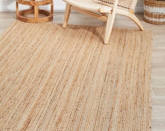 Può includere: Un tappeto in fibra naturale realizzato in juta, un materiale sostenibile e resistente. Il tappeto ha un colore marrone chiaro e una trama tessuta. È un tappeto rettangolare con un bordo leggermente sfilacciato.