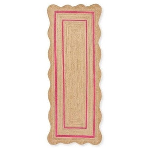 May include: A rectangular jute rug with a scalloped edge and a bright pink border. The rug has a natural, woven texture and a simple, yet elegant design. The rug is perfect for adding a touch of color and texture to any room.