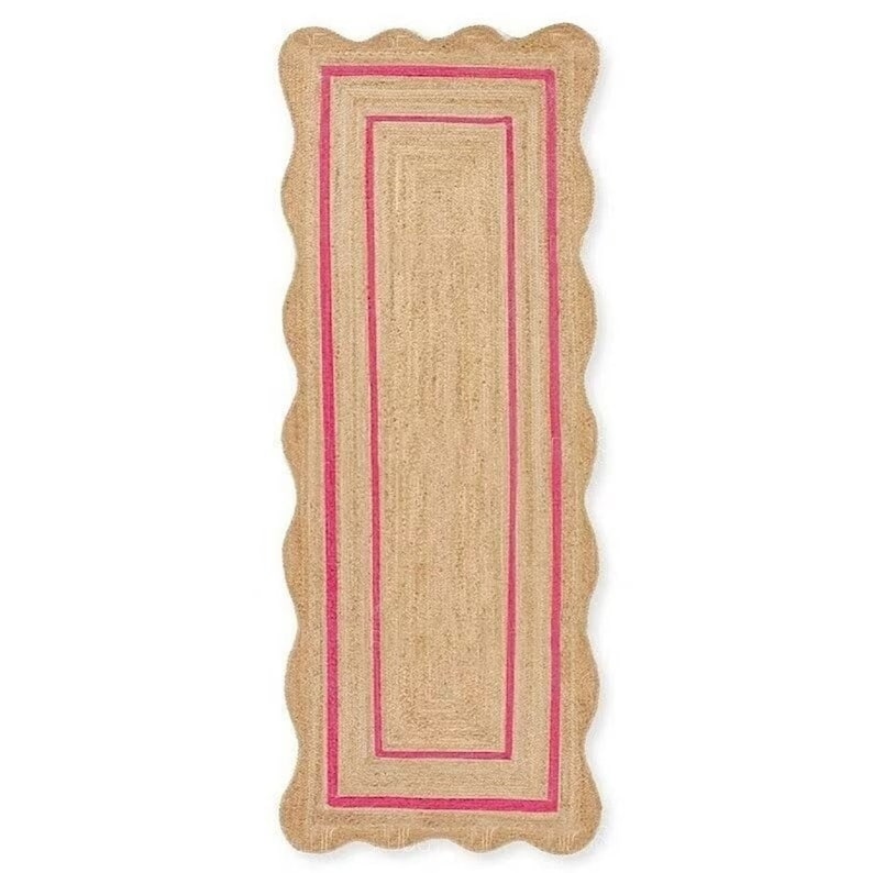 May include: A rectangular jute rug with a scalloped edge and a bright pink border. The rug has a natural, woven texture and a simple, yet elegant design. The rug is perfect for adding a touch of color and texture to any room.