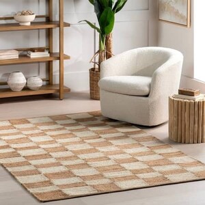 May include: A beige and white checkered jute rug with a white armchair and a wooden side table in the background.