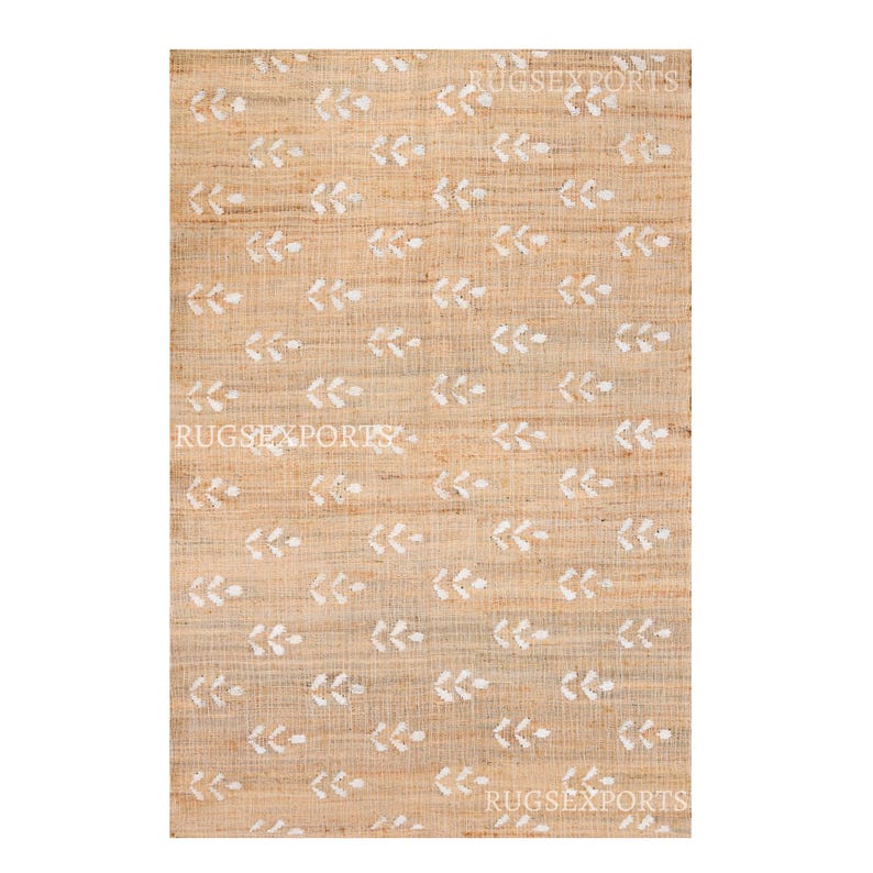 May include: A natural fiber rug with a beige background and a white leaf pattern. The rug has a subtle texture and a simple design.