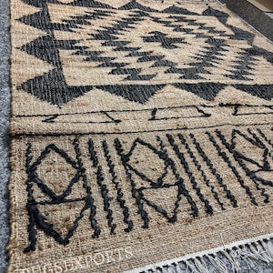 May include: A black and tan jute rug with a geometric pattern. The rug has a fringe border and the text "RUGSEXPORTS" is visible in the bottom left corner.