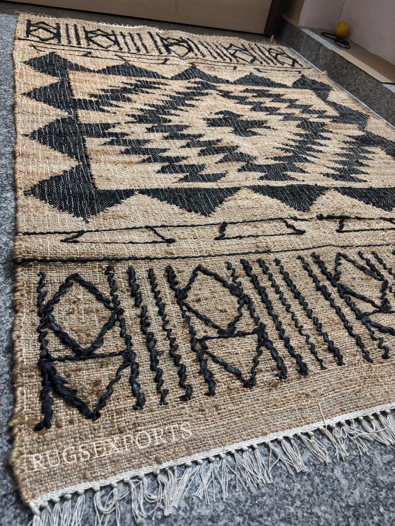May include: A black and tan jute rug with a geometric pattern. The rug has a fringe border and the text "RUGSEXPORTS" is visible in the bottom left corner.