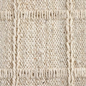 May include: Close-up of a natural fiber rug with a woven texture. The rug has a light beige color and a subtle pattern of diagonal lines.