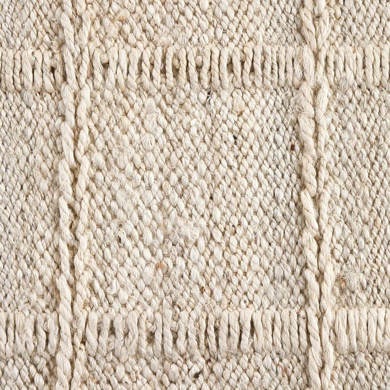 May include: Close-up of a natural fiber rug with a woven texture. The rug has a light beige color and a subtle pattern of diagonal lines.